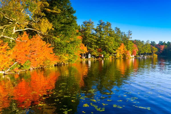 A tranquil lake reflects vibrant autumn foliage under a clear blue sky.