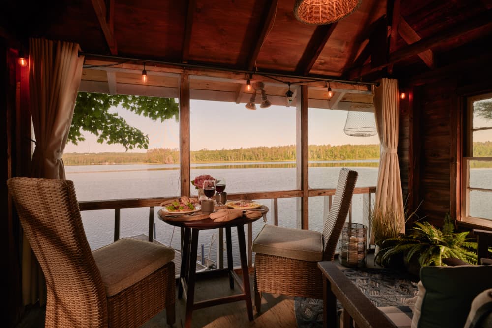 A cozy lakeside dining area with two chairs, a table set with food, and a scenic view of the water and trees.