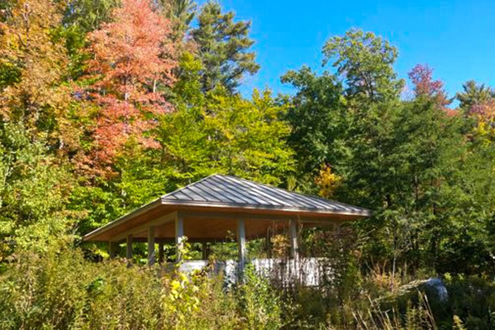 A wooden gazebo surrounded by colorful autumn foliage under a clear blue sky.