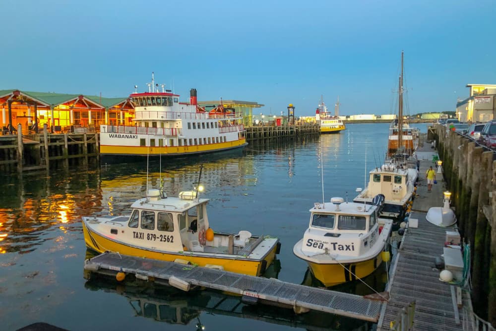 Boats docked at a harbor during sunset, with restaurants lining the waterfront.