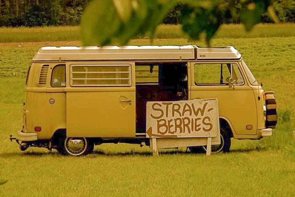 A vintage yellow van parked in a field with a sign announcing "Strawberries."