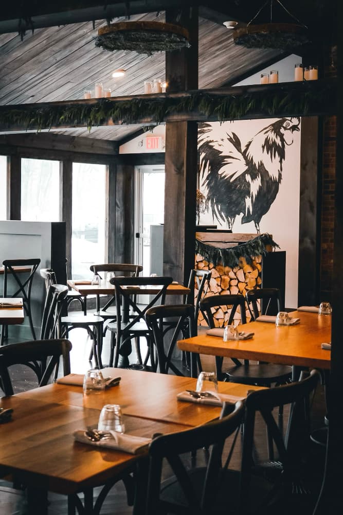 A cozy restaurant interior featuring wooden tables, black chairs, and a large rooster mural.