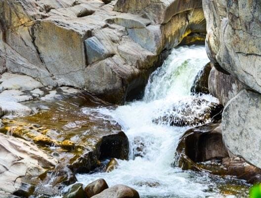 A small waterfall cascades over rocks in a rocky gorge.