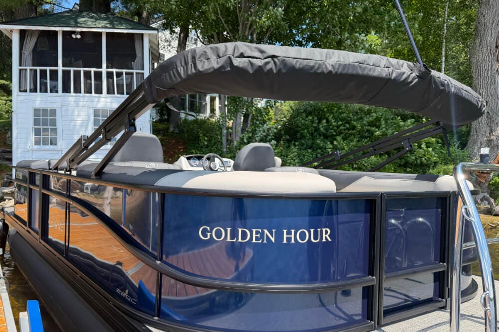 A blue boat named "Golden Hour" docked at a waterfront with trees in the background.