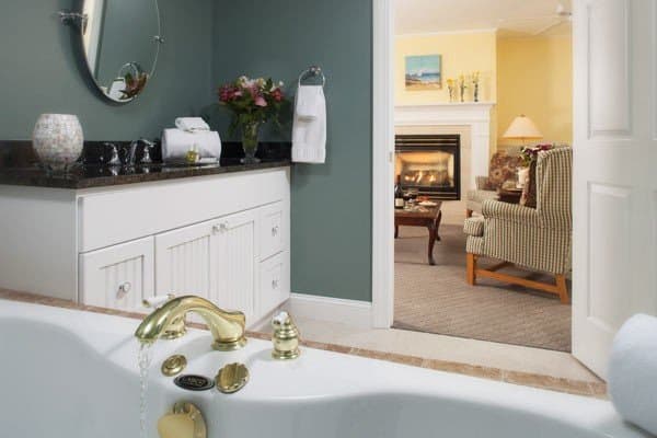 A luxurious bathroom with a gold-finished faucet, leading to a cozy living area featuring a fireplace.