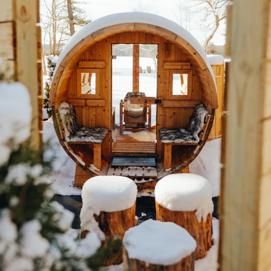 A circular wooden structure with seating inside, surrounded by snow and rustic log stools.
