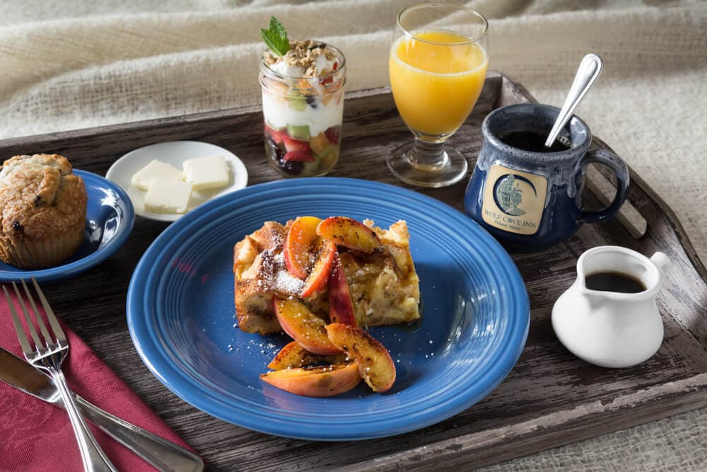 A breakfast tray featuring baked dish with fruit, yogurt parfait, muffin, coffee, orange juice, and butter.