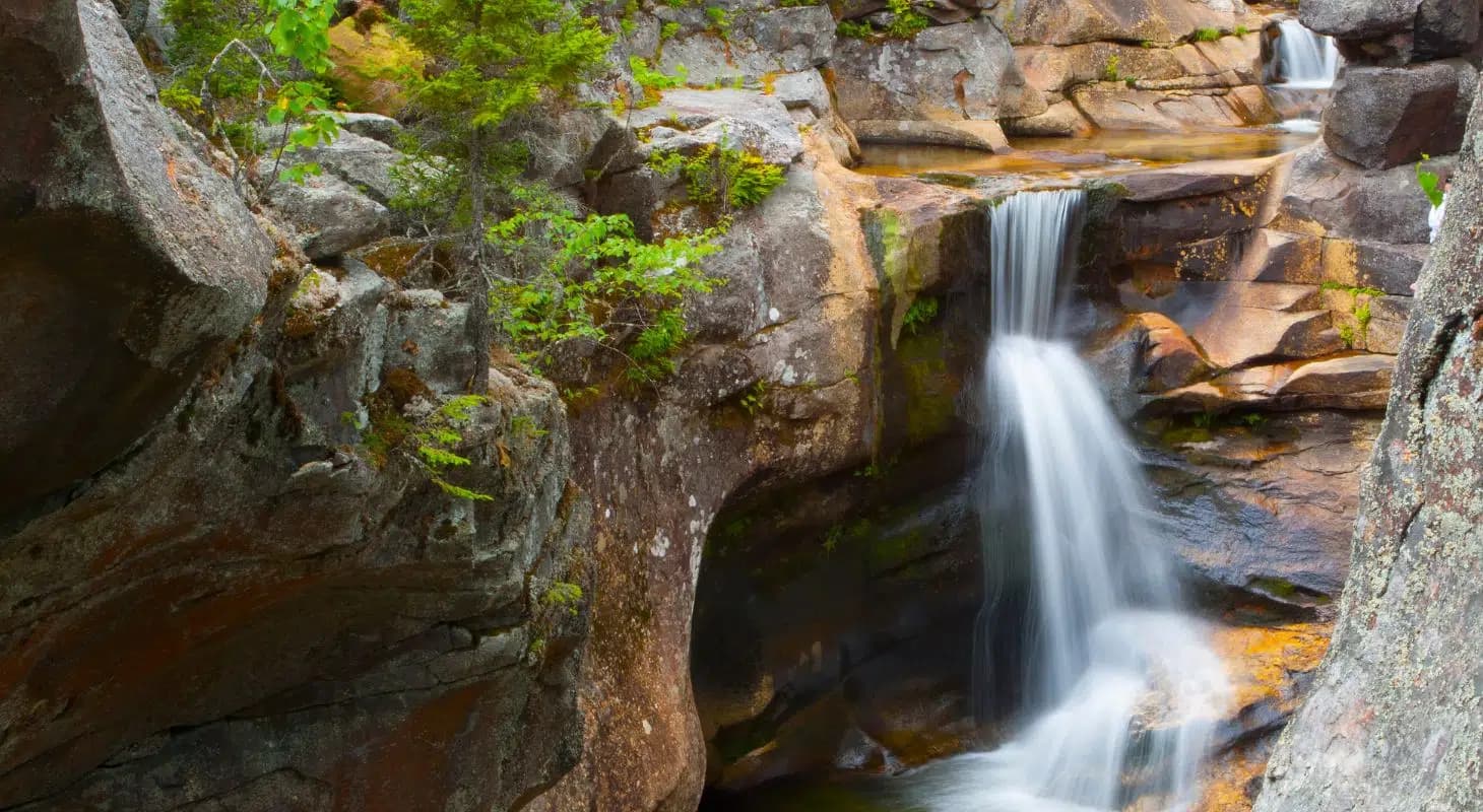 A serene waterfall cascading over rocks, surrounded by lush greenery.