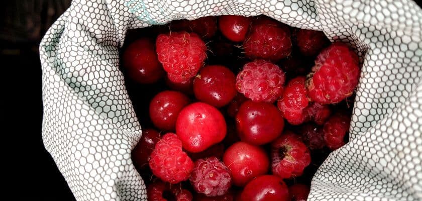 A fabric bag filled with red apples and raspberries.