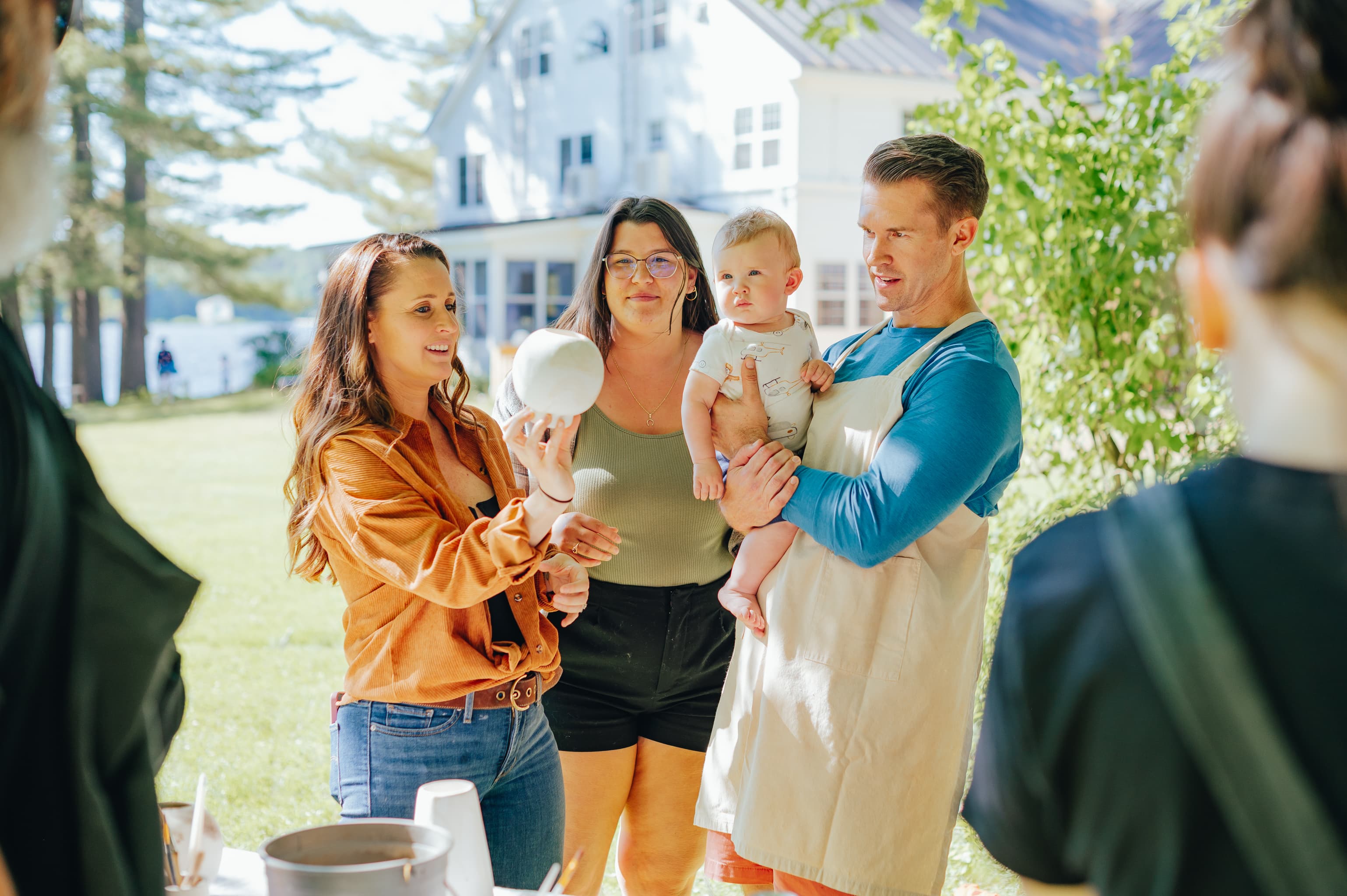 A group of four people, including a baby, engage in a craft activity outdoors near a modern house.