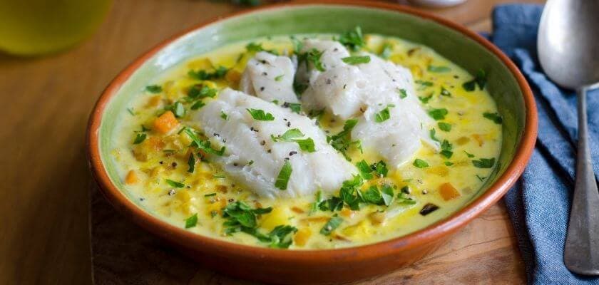 Bowl of fish stew garnished with herbs and vegetables.