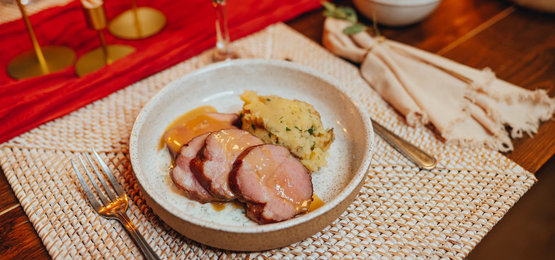 A plate of sliced meat with gravy and a serving of mashed potatoes, presented on a textured table setting.