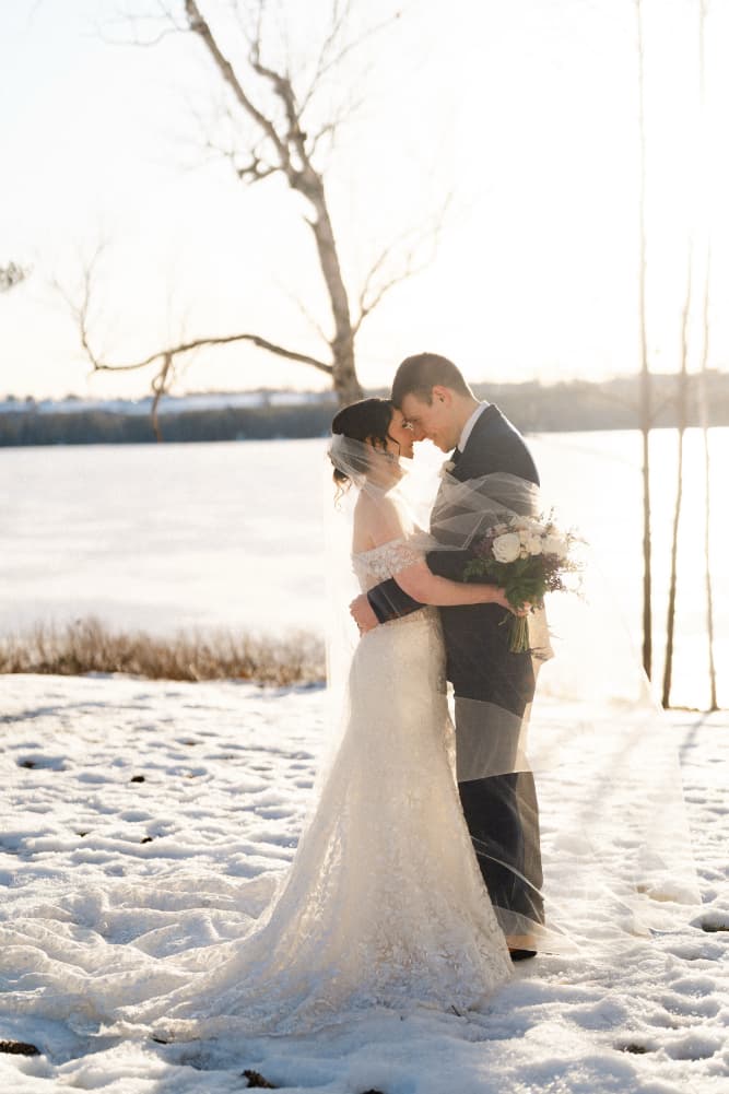 A couple shares a tender kiss on a snowy landscape during sunset.