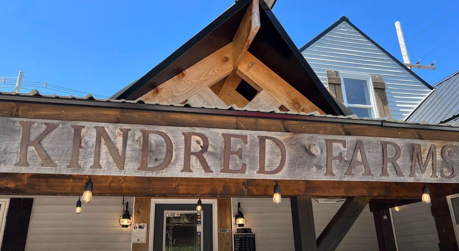 Sign of "Kindred Farms" displayed on a rustic wooden structure under a clear blue sky.