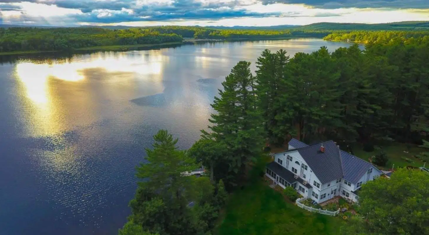 Aerial view of a serene lake bordered by trees, featuring a large white house nearby.