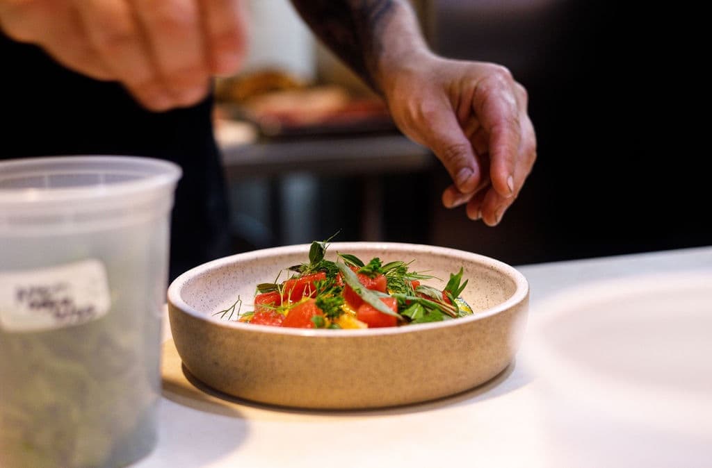 A chef garnishes a colorful dish with fresh herbs in a restaurant kitchen.