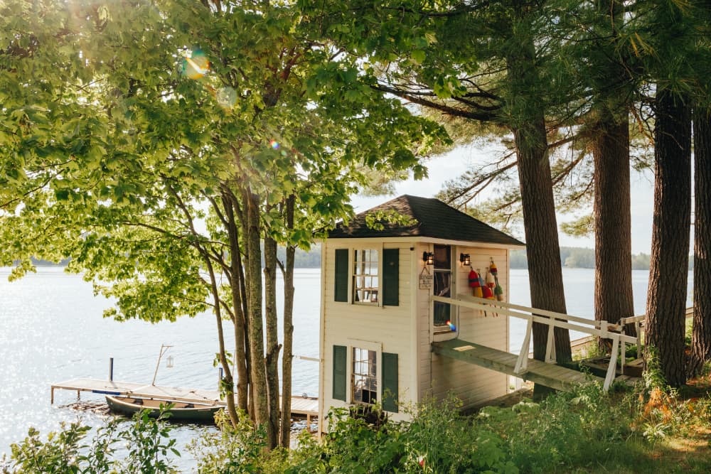 A quaint lakeside cabin surrounded by trees and a shimmering water view.