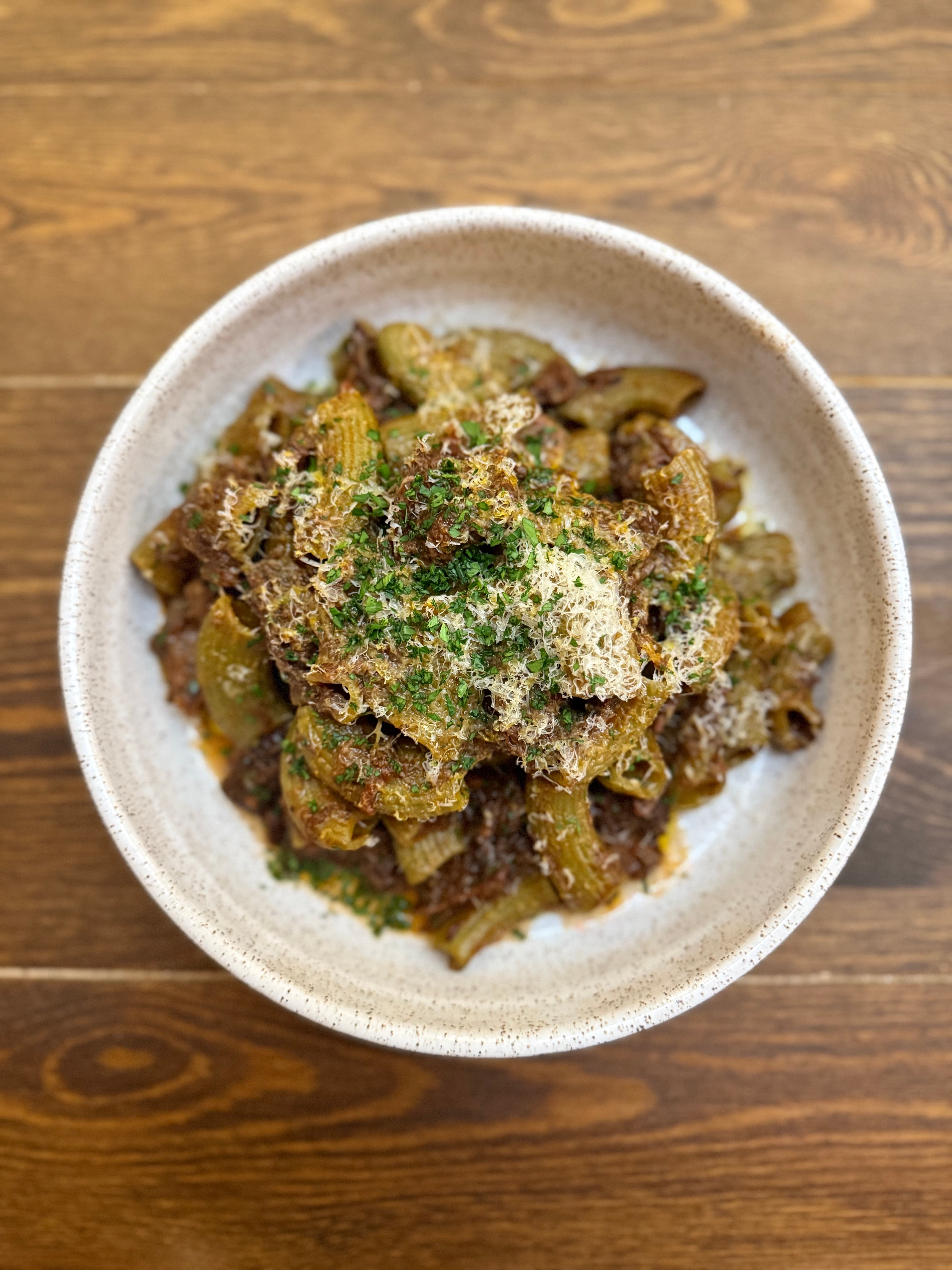 A bowl of rigatoni pasta topped with grated cheese and chopped parsley.