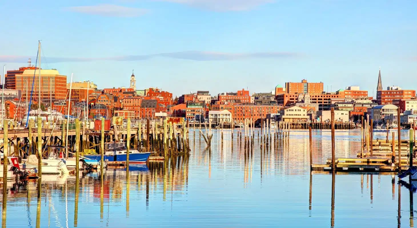 A scenic waterfront view showcasing boats and reflections of buildings along a calm harbor.