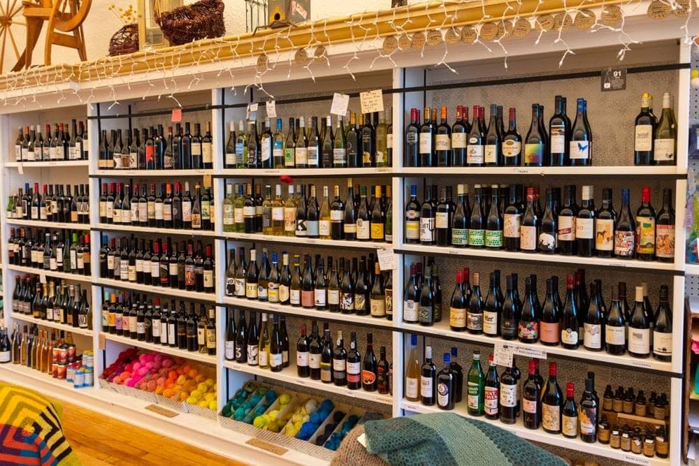 A display of various wine bottles arranged neatly on shelves, with colorful yarn balls below.
