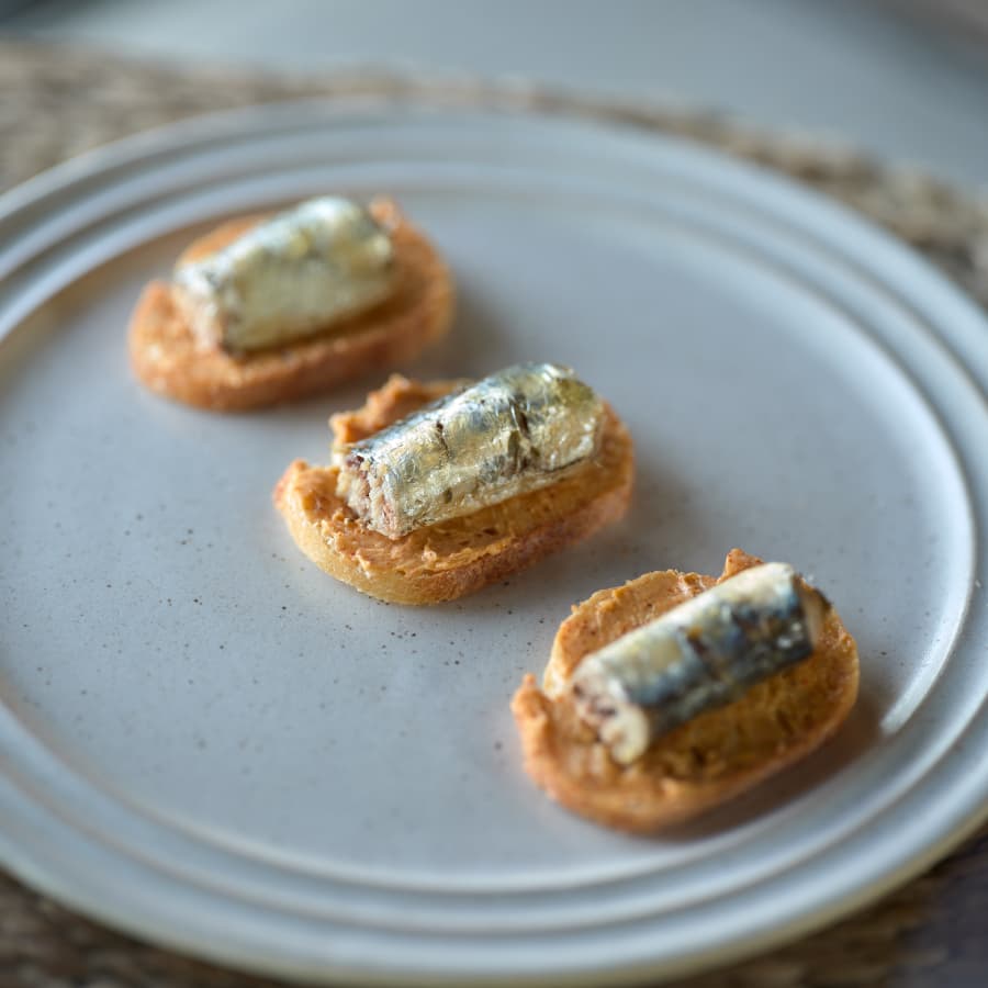 A plate with three toasted crackers topped with sardines.