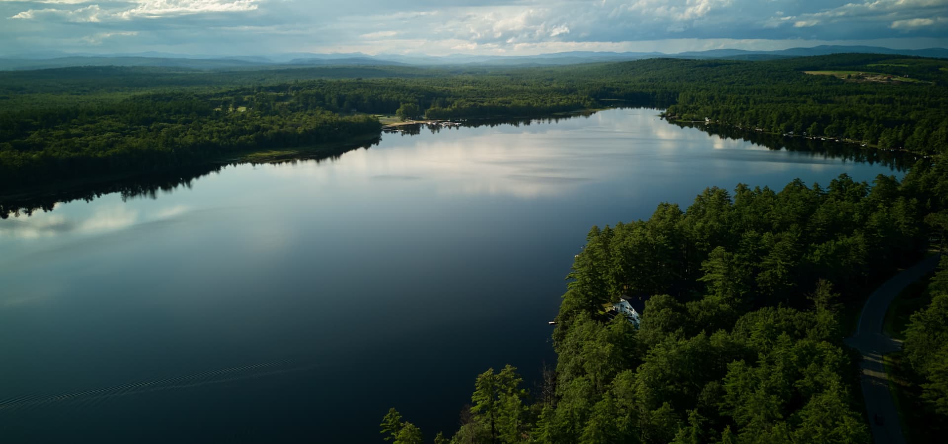 A serene lake surrounded by lush greenery and mountains under a cloudy sky.