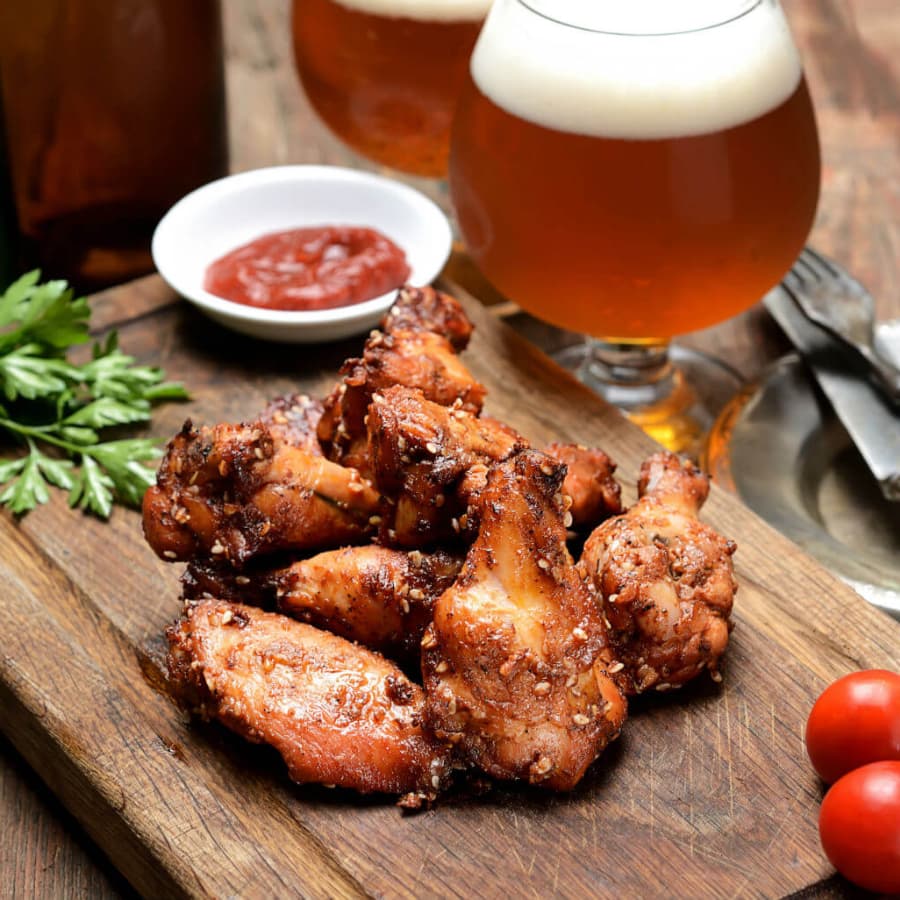 A delicious pile of crispy chicken wings with a side of dipping sauce, garnished with parsley and accompanied by glasses of beer.