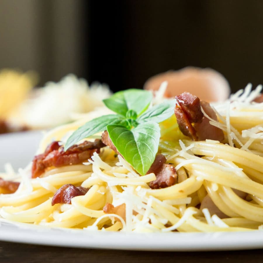A close-up of spaghetti topped with bacon and fresh basil leaves.