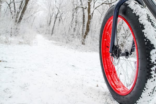 A close-up of a bike tire with a red rim on a snowy, winter trail.