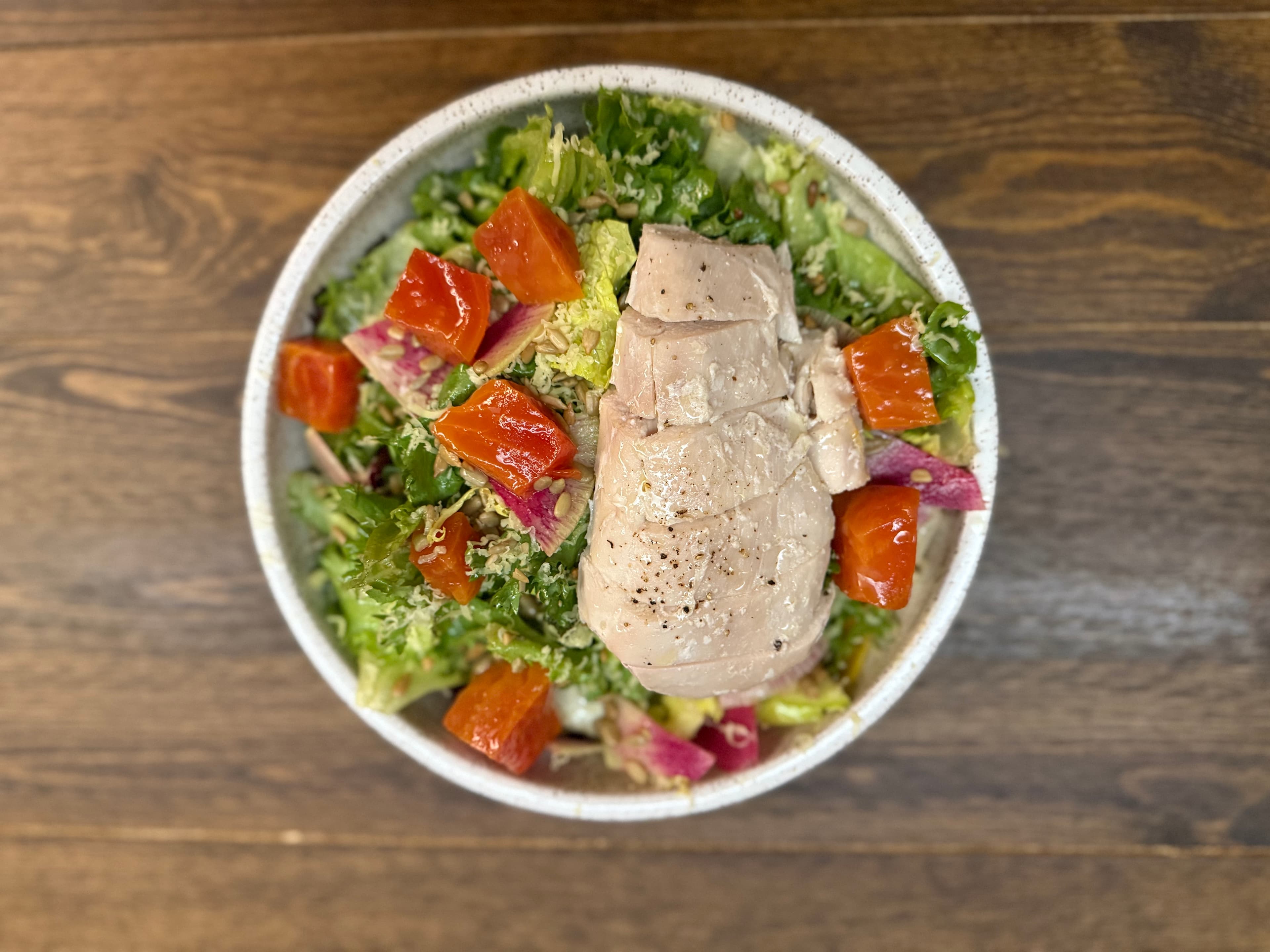 A bowl of salad topped with sliced chicken, colorful tomatoes, and mixed greens.