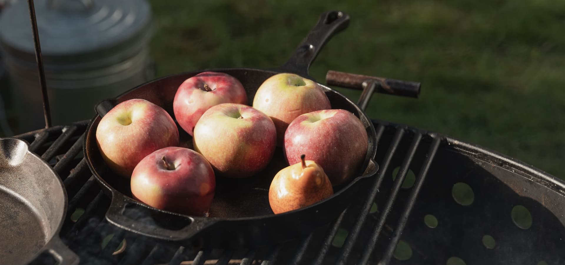 A cast iron skillet holds several red apples on a grill.