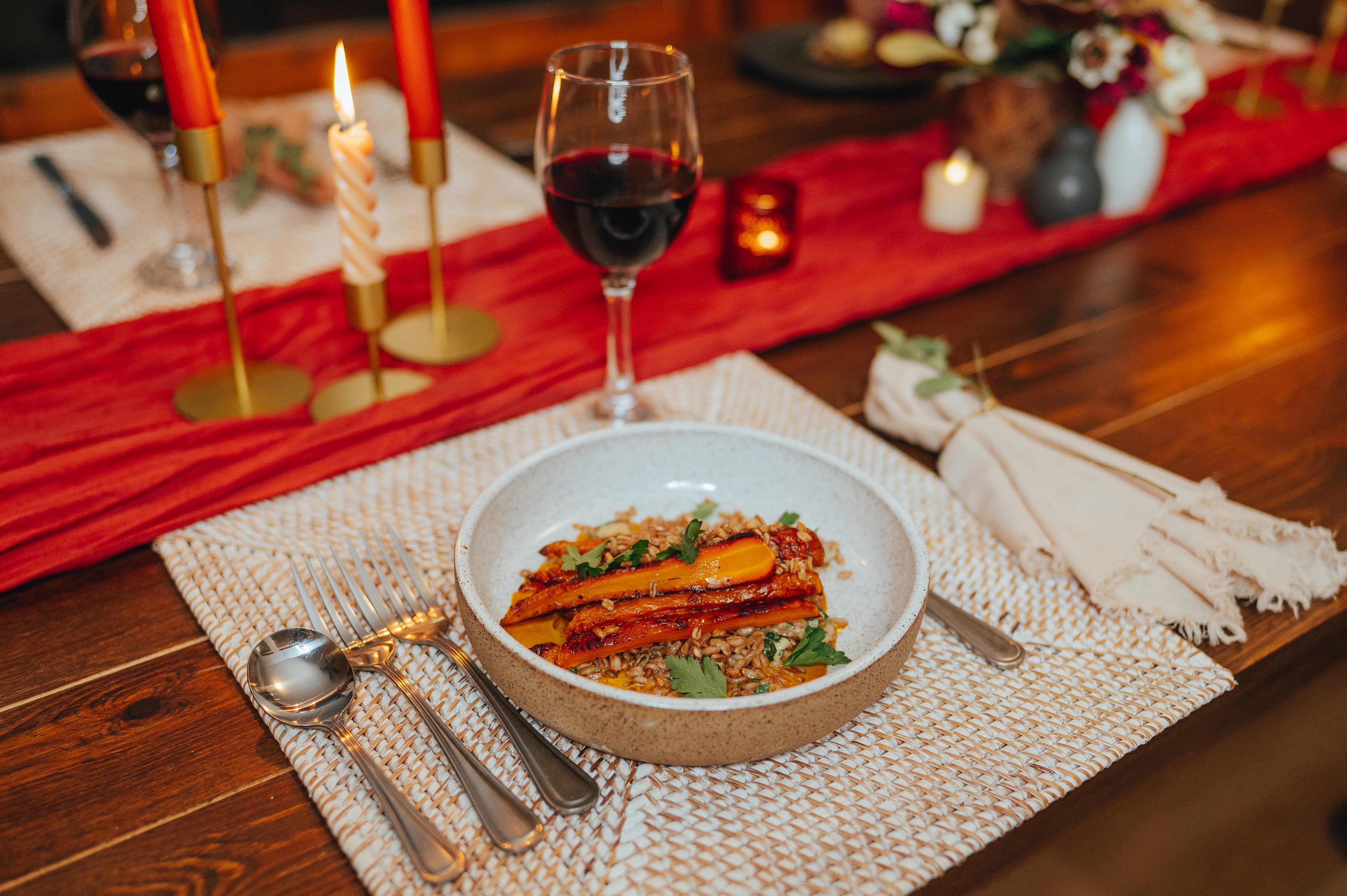 A beautifully arranged table featuring a dish of roasted carrots on grains, accompanied by wine and candles.
