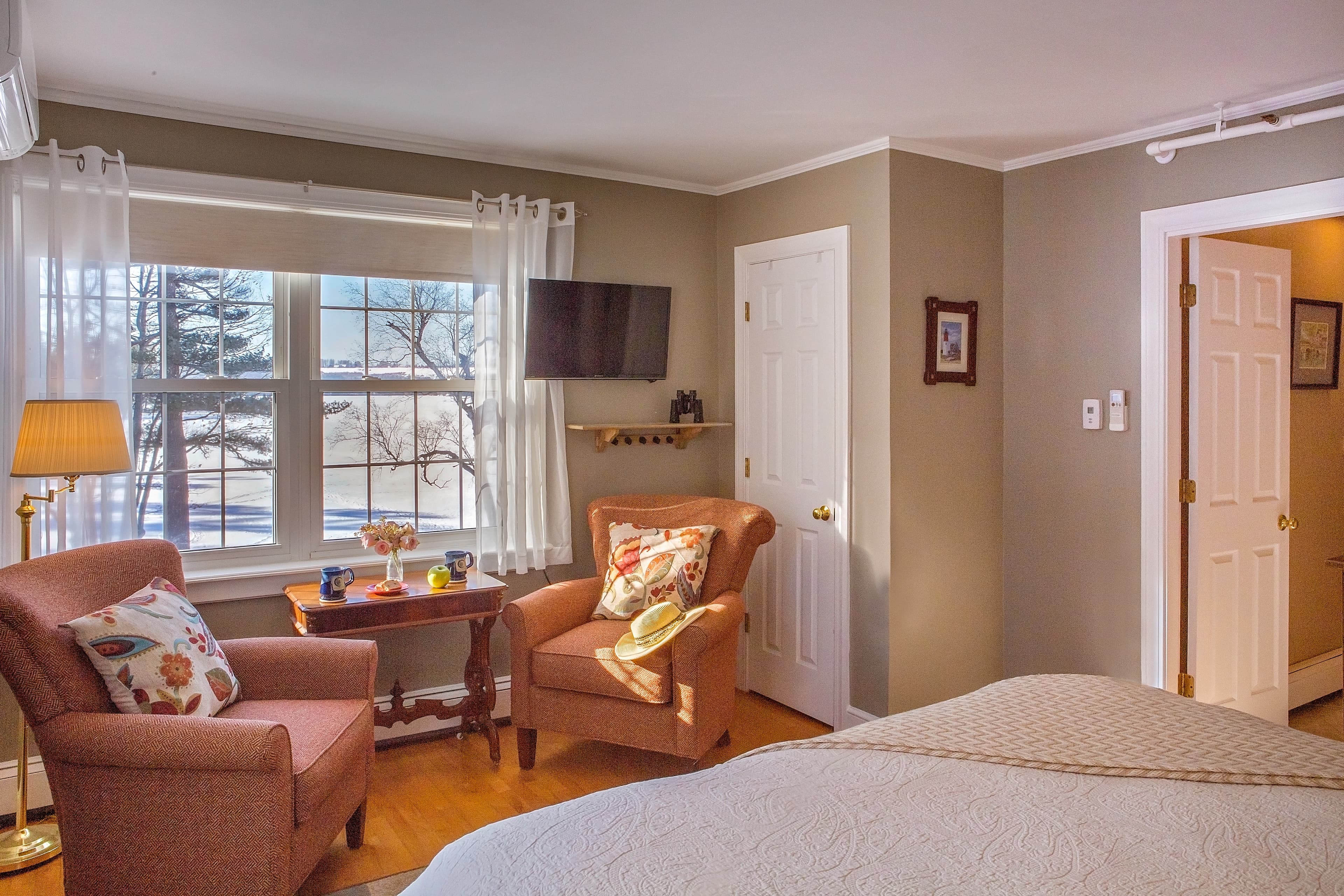 Closeup of the two comfortable chairs set by the lwindow overlooking the lake and flat screen TV as visible from the bed.