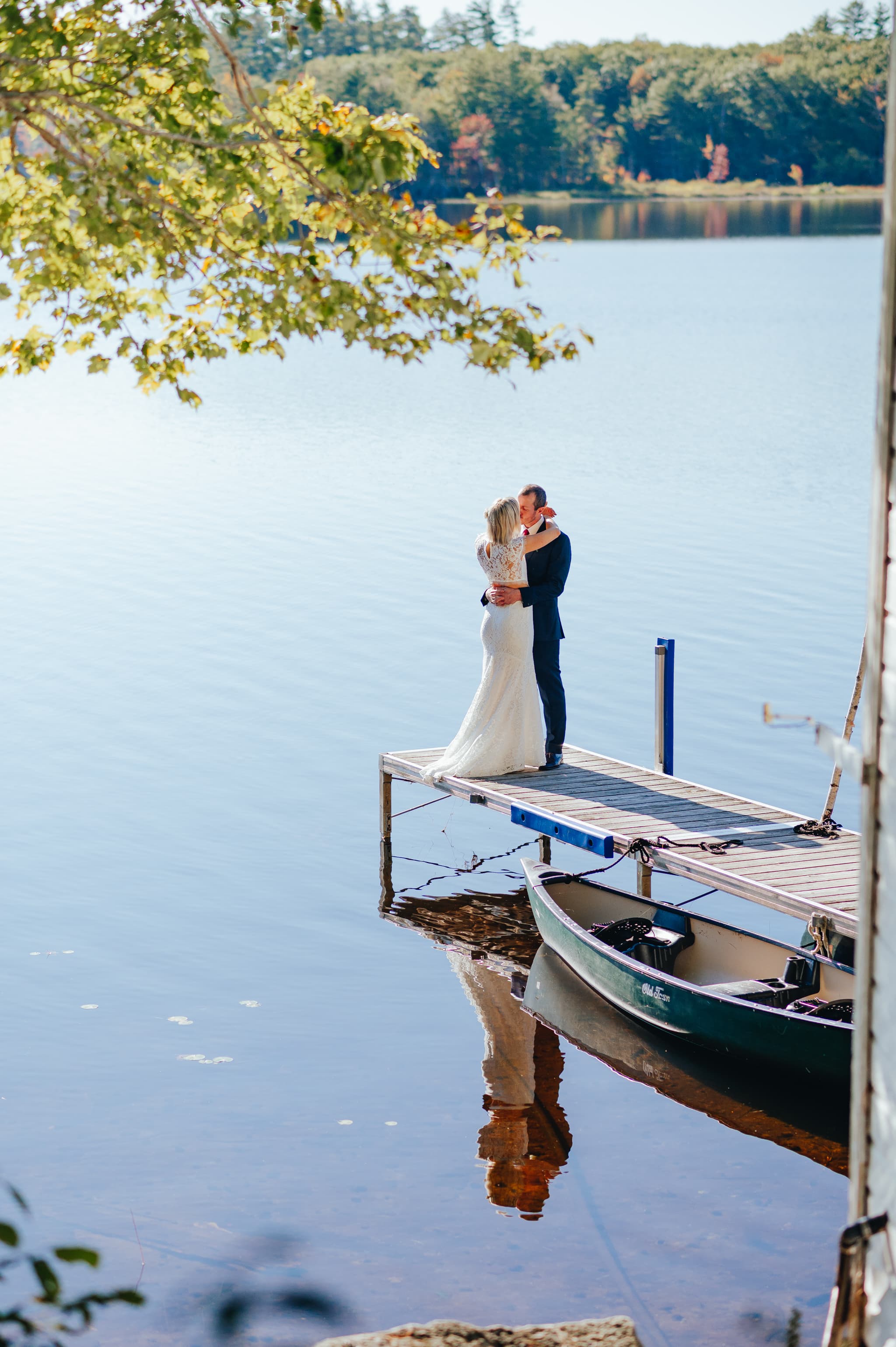 A couple shares a romantic embrace on a dock by a serene lake.