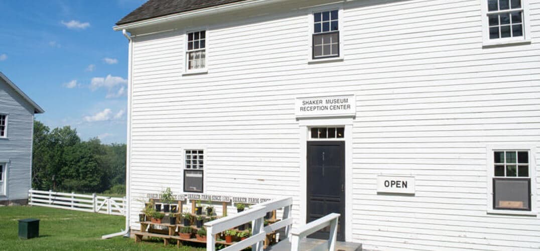 Exterior of the Shaker Museum Reception Center featuring a white wooden building and an "OPEN" sign. Exterior of the Shaker Museum Reception Center featuring a white wooden building and an "OPEN" sign.