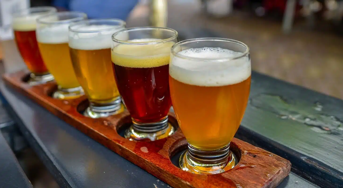 A wooden flight tray holds five glasses of different beers.