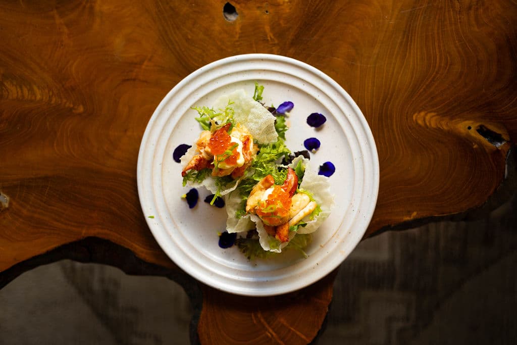 A plate of lettuce wraps with shrimp, garnished with greens and edible flowers, on a wooden table.