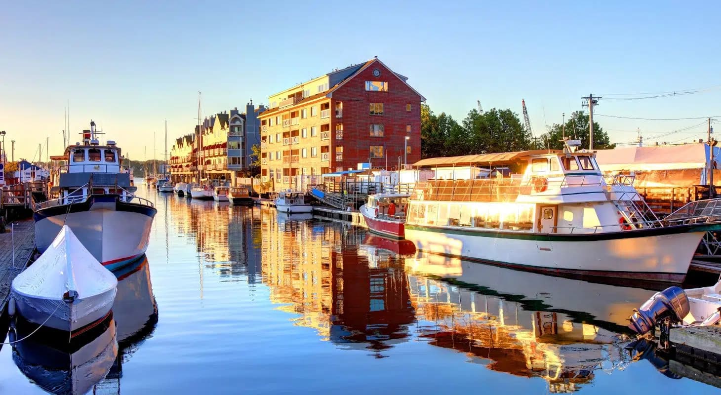 A peaceful marina at sunrise with boats reflecting on calm water beside a waterfront building.