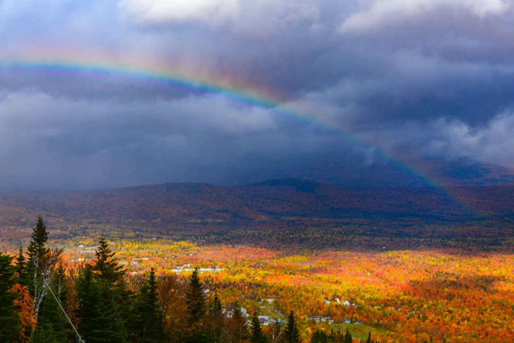 A vibrant rainbow arches over a colorful autumn landscape.