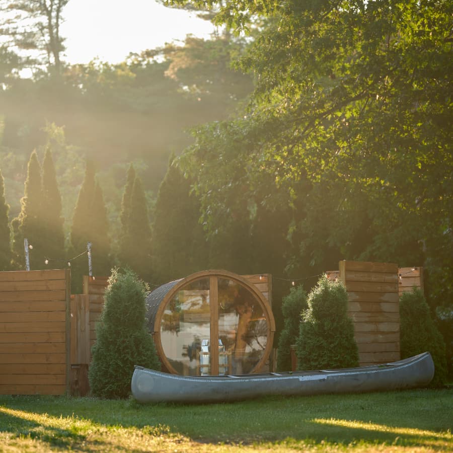 A canoe resting on green grass near wooden structures and trees in a softly lit outdoor setting.