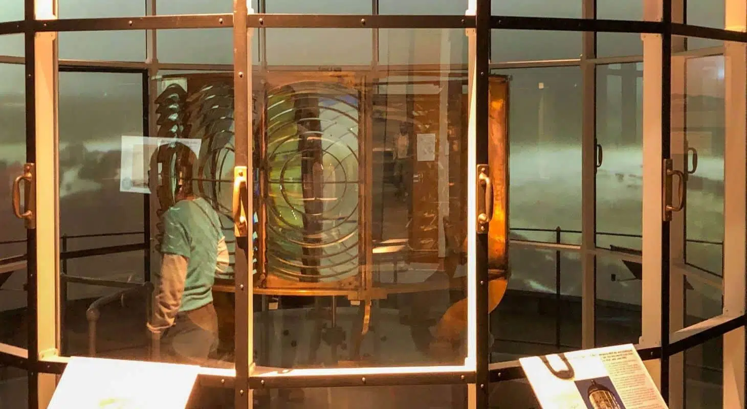 A person examines an exhibit featuring a historical lighthouse lens behind glass.