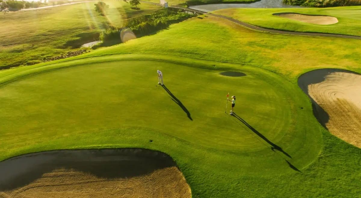 a golfer is putting the ball into the hole while another player holds the flag