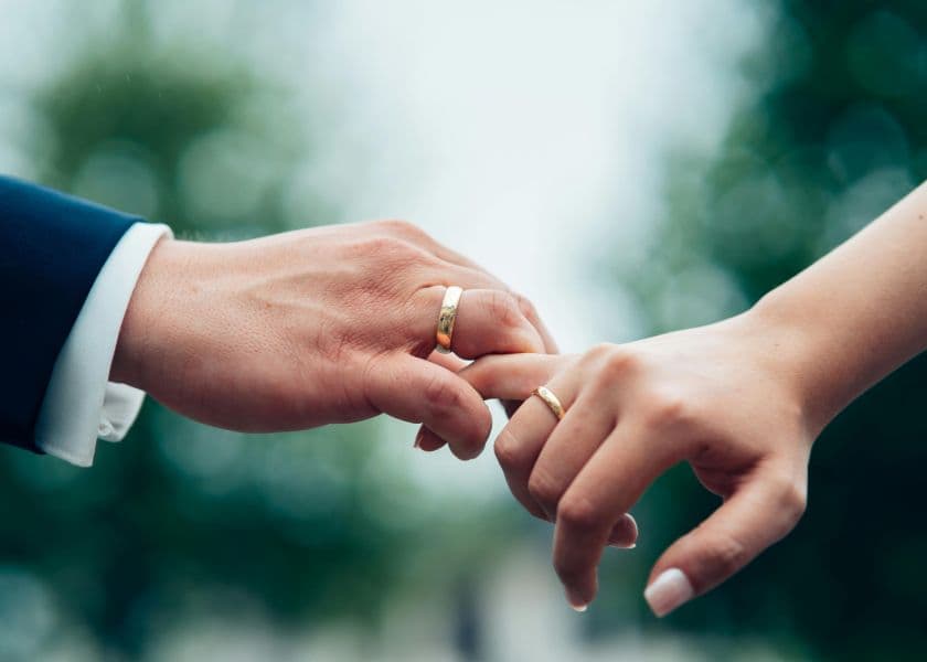 A close-up of a bride and groom holding hands with wedding rings in soft outdoor light. A close-up of a bride and groom holding hands with wedding rings in soft outdoor light.