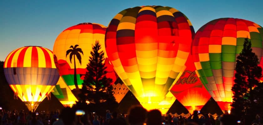 colorful hot air balloons glowing at night with a crowd of people watching