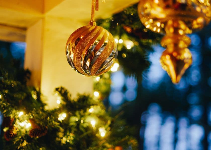 closeup of a gold striped christmas ornament hanging above glowing garland with warm holiday lights