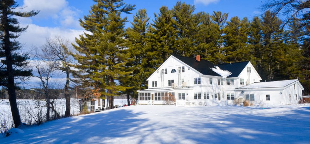 White clapboard inn set among towering pines on a winter landscape of snow.