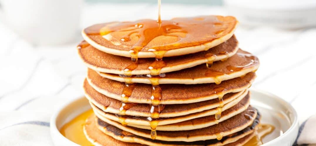 A large stack of pancakes with a healthy serving of maple syrup poured over top