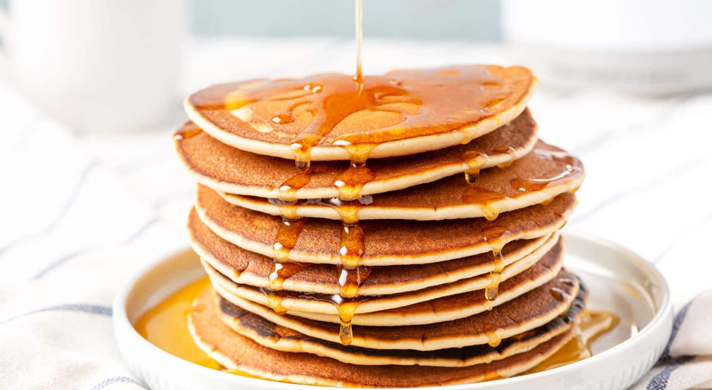 A large stack of pancakes with a healthy serving of maple syrup poured over top