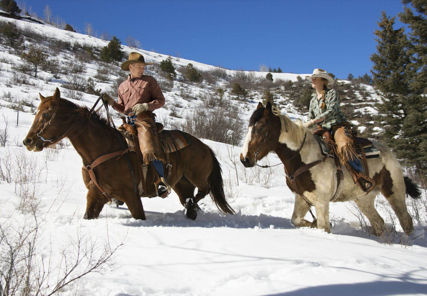 Man and woman riding horses through snow