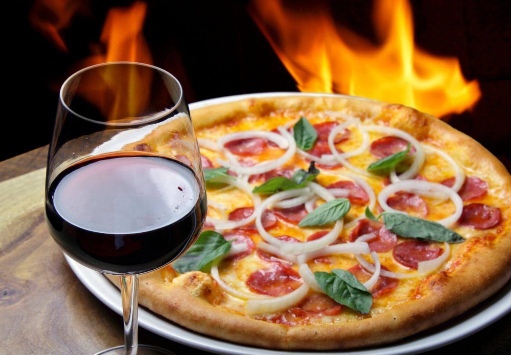 Fancy pizza near fire oven with wine glass